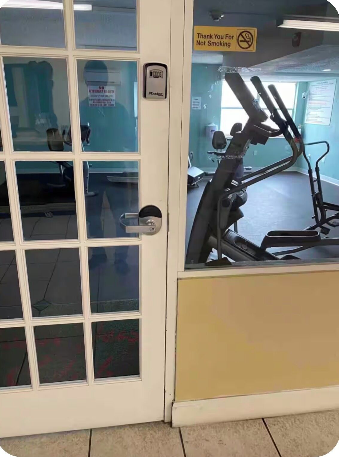 Una porta con un pannello di vetro, un cartello con la scritta 'Grazie per non fumare' e una cyclette all'interno.