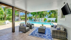 A covered patio with wicker furniture, a pool, and a TV mounted on the wall. - The Gardens- Private Pool (Miami Gardens)