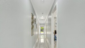 A hallway with white walls and a marble floor leading to a door. - The Gardens- Private Pool (Miami Gardens)