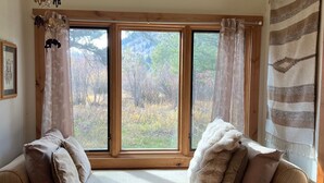 A room with a large window, wooden beams, a hanging light fixture, and a view of trees.