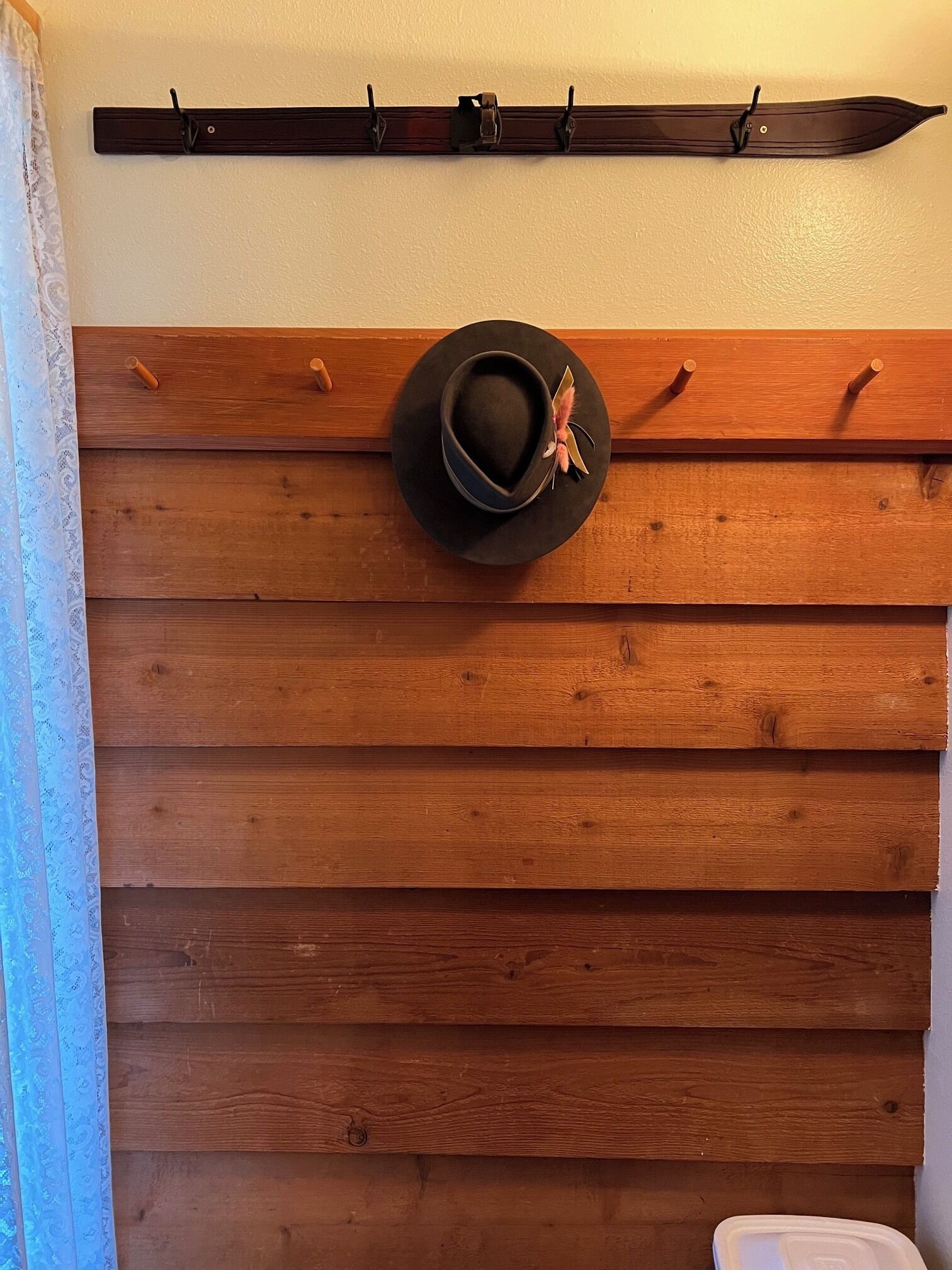 A wall with a wooden panel design, a black hat with a feather, and a coat rack above.
