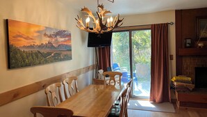A dining area with a wooden table and chairs, a mounted TV, and a painting of a mountain landscape.