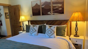 A neatly made bed with a green bedspread and patterned pillows, a wooden headboard, and two bedside lamps.