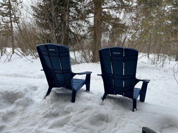 Two blue Adirondack chairs in a snowy outdoor setting.