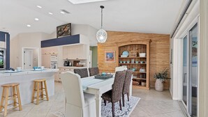 Une cuisine moderne dotée d’un îlot central, de meubles en bois et d’un coin repas avec une table blanche et des chaises à motifs.