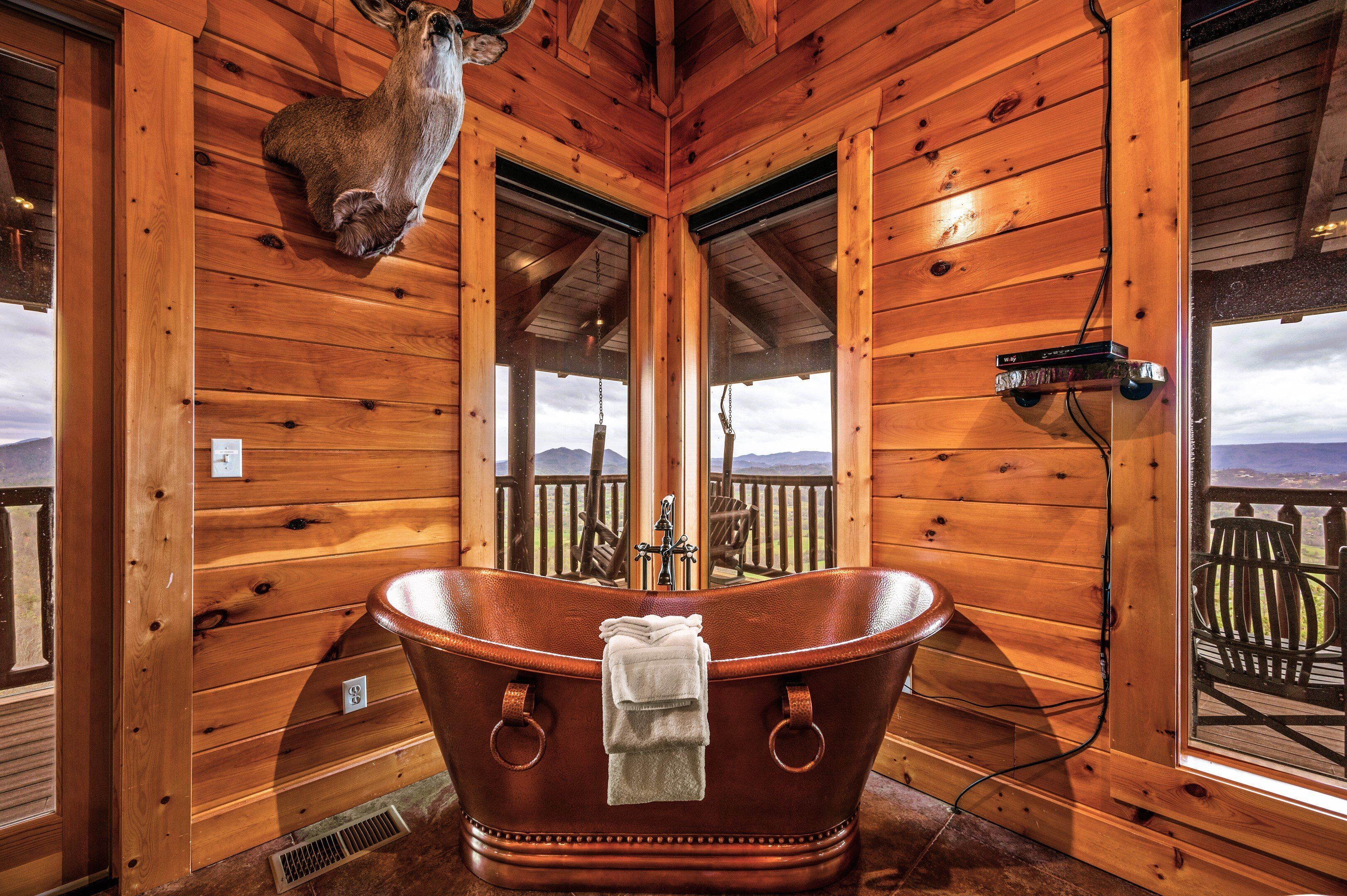 Ein Holzblockhaus-Interieur mit einer großen Badewanne, einem aufgehängten Hirschgeweih und Blick auf Berge durch die Fenster.