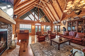 Un intérieur spacieux de chalet en bois, avec un plafond haut, des murs en bois, une cheminée, des meubles en cuir et un grand lustre.