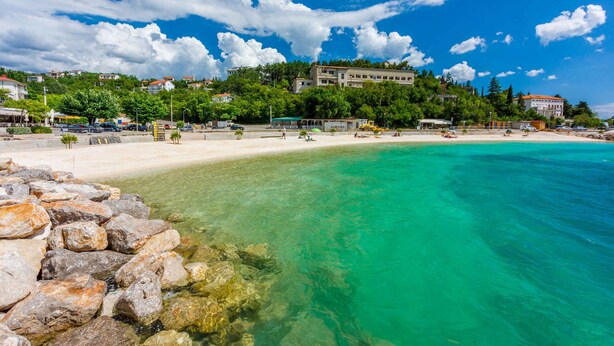 Una spiaggia con acque cristalline turchesi, una riva sabbiosa e edifici sullo sfondo.