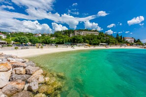 A beach with clear turquoise water, a sandy shore, and buildings in the background. - Holiday home tastefully decorated with swimming pool (Jadranovo)