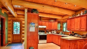 L’intérieur d’une cabane en bois comprend un coin cuisine avec des meubles de rangement en bois, un poêle et un évier.