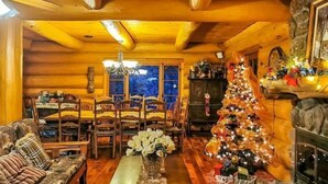 L’intérieur d’un chalet confortable, avec des murs en rondins de bois, une table à manger en bois, des chaises, un canapé, un sapin de Noël et une cheminée en pierre.