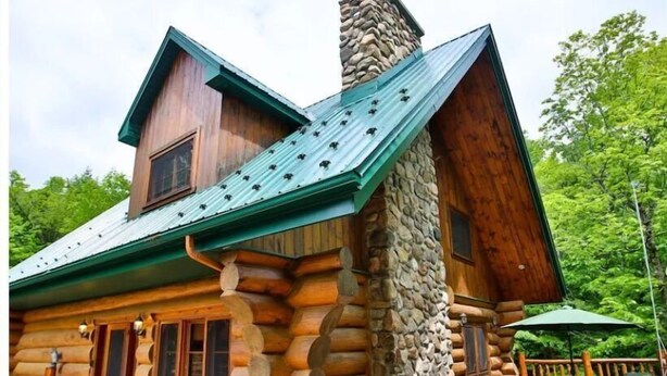Une cabane en rondins avec une cheminée en pierre, un revêtement extérieur en bois et une terrasse dotée de chaises longues et d’un barbecue.