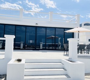 Un espace extérieur moderne, aménagé avec des sièges, des marches blanches menant à une porte vitrée, des tables et des chaises d’extérieur.