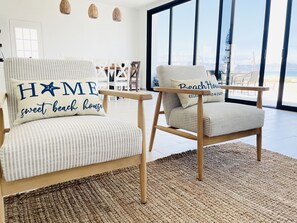 Uma sala de estar moderna com duas cadeiras, uma com uma almofada com a inscrição 'CASA doce casa de praia' e outra com a inscrição 'Casa de Praia'.