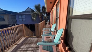 A wooden deck with two light blue chairs and a table, a wooden railing, and a building with a window and a door. - LOCATION! LOCATION! LOCATION! WEST BEACH Public Access across from complex (Gulf Shores)