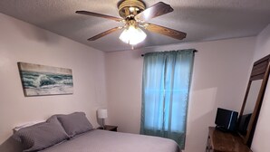 A bedroom with a bed, a ceiling fan, a painting, a window with curtains, and a dresser with a TV. - LOCATION! LOCATION! LOCATION! WEST BEACH Public Access across from complex (Gulf Shores)