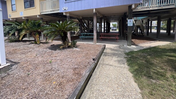 A building with a covered patio area, outdoor seating, and a sign indicating a designated smoking area. - LOCATION! LOCATION! LOCATION! WEST BEACH Public Access across from complex (Gulf Shores)