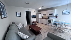 A living room with a grey sofa, a wooden coffee table, and a dining area with a small table and chairs. - LOCATION! LOCATION! LOCATION! WEST BEACH Public Access across from complex (Gulf Shores)