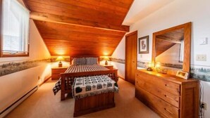 Ein Schlafzimmer mit schrägemausertem Dach, Holzmöbeln, einem Bett mit karierter Bettdecke, einem Schminktisch und einem Spiegel.