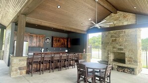 A covered outdoor kitchen area with a stone fireplace, wooden bar, and seating. - Come Relax at THE CROW'S NEST , Patriot Pointe at Lake Eufaula.  (Eufaula)