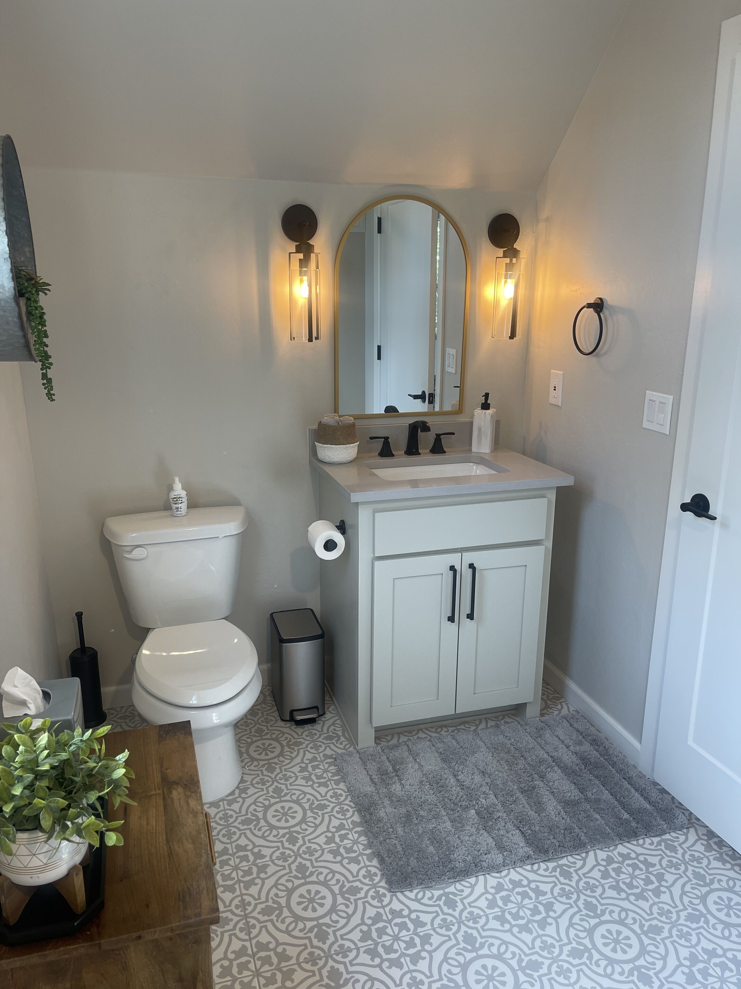 Une salle de bain  équipée de toilettes, d’un lavabo, d’un miroir et d’un carrelage décoratif.