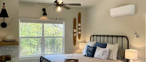 A bedroom with a bed, bedside table, lamp, and a window with a view of trees.