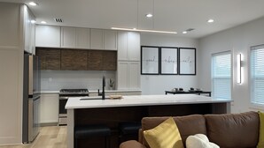 Eine moderne Küche mit weißen Schränken, einer zentralen Kochinsel und einem Essbereich mit braunem Sofa und Kissen.