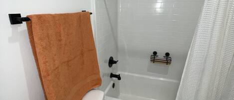 Un baño con inodoro blanco, bañera y cortina de ducha.