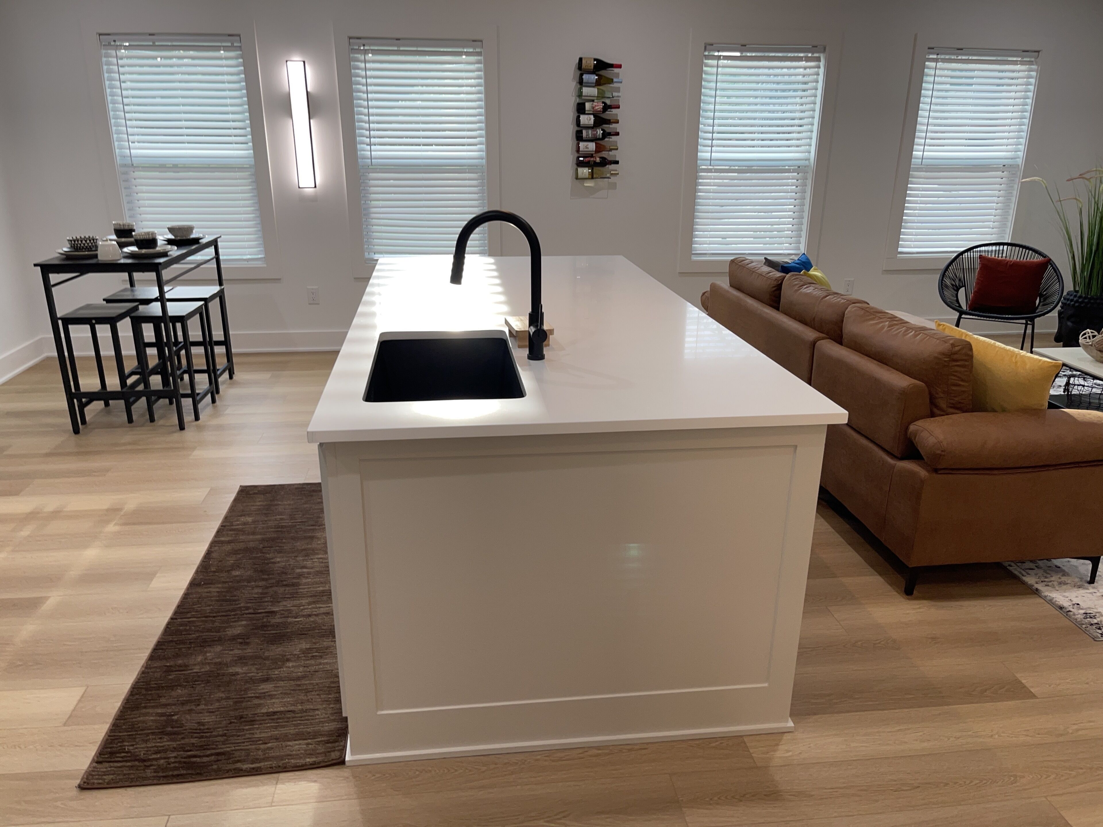 A modern kitchen with a central island, a dining area with a black metal table and chairs, and a brown leather sofa.