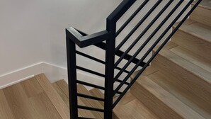 Eine Treppe mit schwarzer Metallreling und Holzbodenstufen.