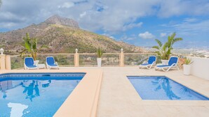 Une piscine sur le toit, divisée en deux zones, avec des chaises longues bleues, des plantes en pot et une vue imprenable sur les montagnes.