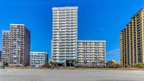 A high-rise building with multiple balconies, a flat roof, and a clear blue sky.