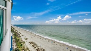 A beach with a clear view of the ocean and a building with a balcony overlooking the beach.