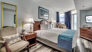 A hotel room with a bed, bedside tables, a chair, a mirror, a window with curtains, and a television.