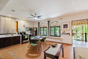 A modern kitchen with a dining area, large windows, and a ceiling fan. - Stylish jungle studio retreat with a veranda, parking & full kitchen. For 2-3 (Quepos)