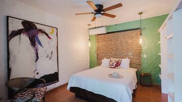 Un dormitorio con cama, ventilador de techo, aire acondicionado en la pared y un cuadro abstracto de gran tamaño.