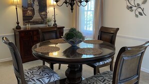 Ein Esszimmer mit einem runden Tisch, vier Stühlen, einer Kandelaber, einem Wanddekor und einem Wandbild.