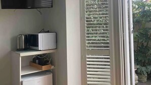 Ett rum med en platt-TV som är monterad på väggen, en mikrovågsugn och ett kylskåp. Det finns en skjutdörr i glas som leder ut till ett utomhusområde med grönska.