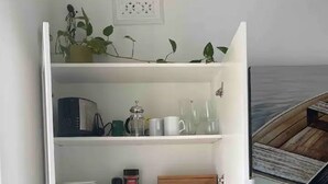Ett litet rum med ett vitt skåp som innehåller köksutrustning, ett litet bord med en stol och en säng med ett blått överkast.