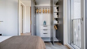 A modern bedroom with a large bed, a walk-in closet with hanging clothes, and a view through a sliding glass door. - Remarkable Wiedikon 2BR w/ Storage & W/D, nr Market, by Blueground (Zurich)