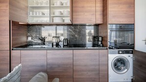 A modern kitchen with wooden cabinets, a black marble backsplash, and built-in appliances including a washing machine and a stove. - Remarkable Wiedikon 2BR w/ Storage & W/D, nr Market, by Blueground (Zurich)