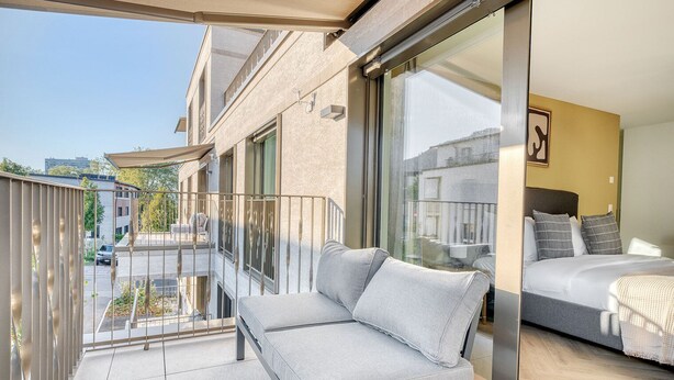 A balcony with a sofa and a bed in the adjacent room. - Remarkable Wiedikon 2BR w/ Storage & W/D, nr Market, by Blueground (Zurich)
