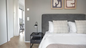 Un dormitorio con cama, mesita de noche, lámpara y una obra de arte en la pared.