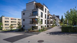Un moderno edificio residencial de varios pisos con balcones, un camino pavimentado y cielo despejado.