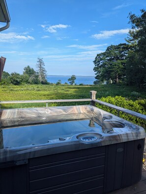 Un jacuzzi en una terraza con vista al mar y vegetación.
