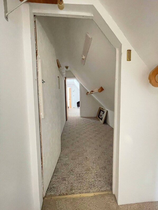 Una escalera estrecha alfombrada que lleva a una habitación con paredes blancas y una puerta de madera.