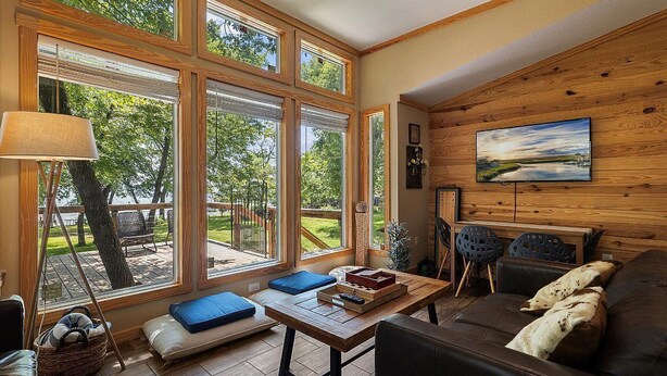 A cozy living room with large windows, a wooden wall, and a comfortable seating area.