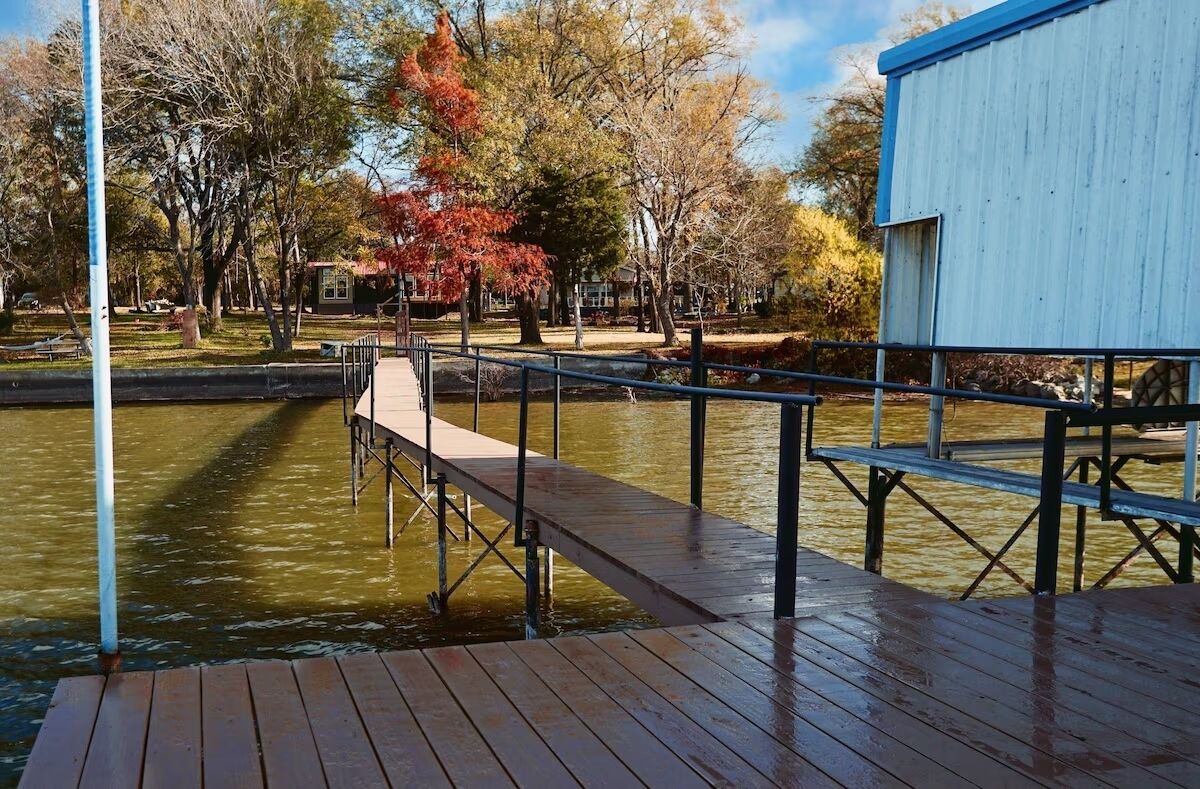 A wooden dock extending over a body of water, with a metal railing and a small building in the background.