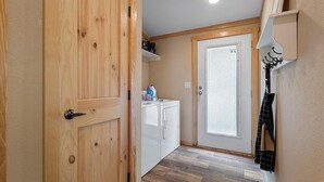A hallway with a wooden door, a white laundry room, and a coat rack.