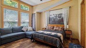 A bedroom with a bed, a sofa, a nightstand, and a window with blinds.